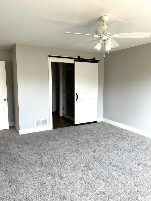 unfurnished bedroom featuring visible vents, a barn door, baseboards, and carpet floors
