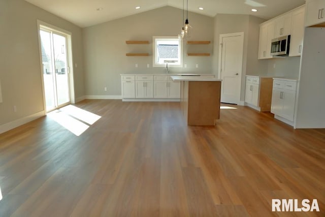 kitchen with stainless steel microwave, a kitchen island, light wood-type flooring, white cabinets, and open shelves