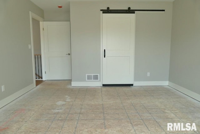 unfurnished bedroom with visible vents, baseboards, and a barn door