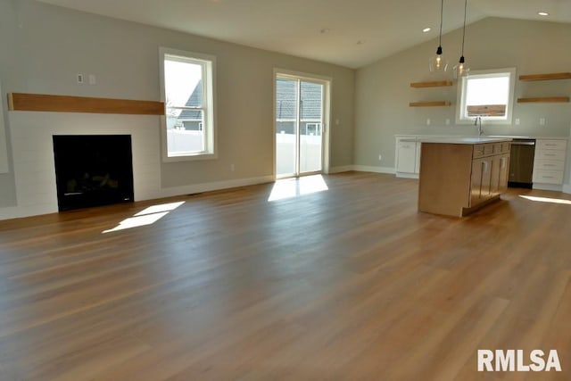 unfurnished living room featuring wood finished floors, baseboards, a fireplace, a sink, and vaulted ceiling