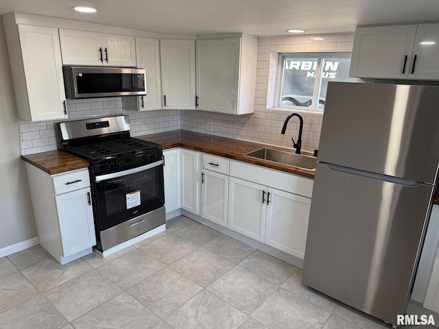 kitchen with butcher block countertops, a sink, backsplash, stainless steel appliances, and white cabinets