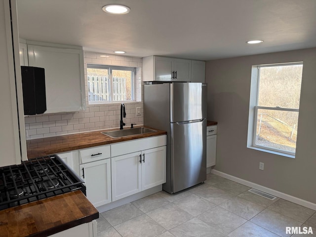 kitchen with a wealth of natural light, decorative backsplash, freestanding refrigerator, wood counters, and a sink