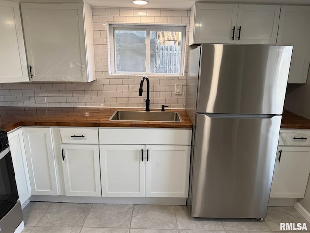 kitchen with tasteful backsplash, wooden counters, freestanding refrigerator, white cabinets, and a sink