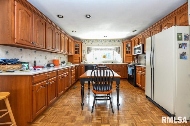 kitchen with brown cabinets, black appliances, a sink, light countertops, and glass insert cabinets