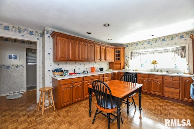 kitchen with wallpapered walls, brown cabinetry, and visible vents