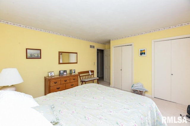 bedroom featuring light carpet, visible vents, and multiple closets