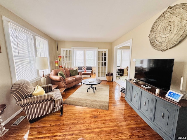 living area with visible vents, a healthy amount of sunlight, baseboards, and wood finished floors