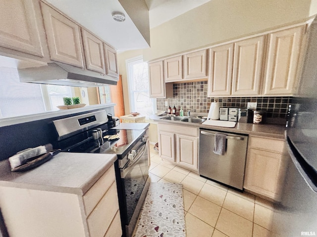 kitchen featuring light tile patterned flooring, a sink, decorative backsplash, under cabinet range hood, and appliances with stainless steel finishes