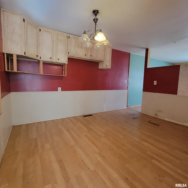 unfurnished room with wainscoting, visible vents, light wood-style flooring, and an inviting chandelier