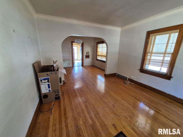 spare room featuring baseboards, arched walkways, wood finished floors, and ornamental molding