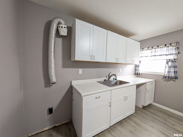 kitchen featuring light wood-type flooring, a sink, white cabinets, light countertops, and baseboards