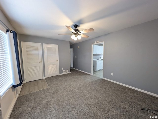 unfurnished bedroom with visible vents, two closets, baseboards, carpet flooring, and a ceiling fan