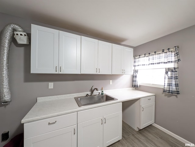 washroom with a sink, baseboards, cabinet space, and light wood-style flooring