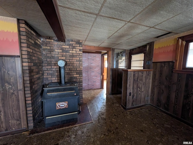 unfurnished living room featuring a paneled ceiling, bar area, wood walls, and a wood stove