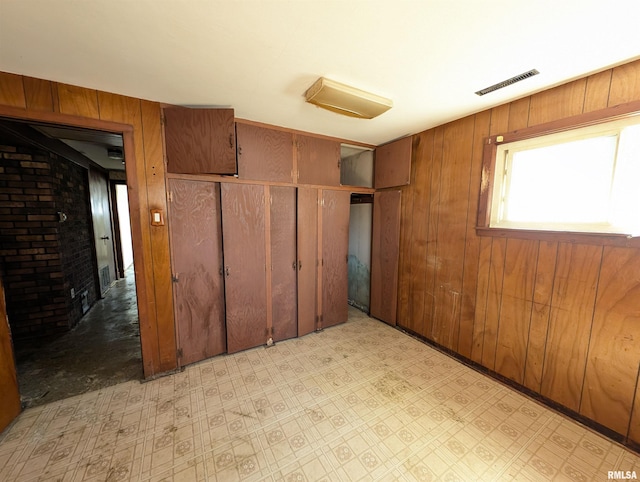 unfurnished bedroom with visible vents, light floors, a closet, and wood walls