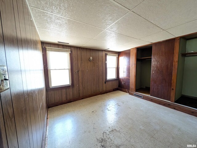 unfurnished bedroom with wooden walls, baseboards, a drop ceiling, a closet, and tile patterned floors