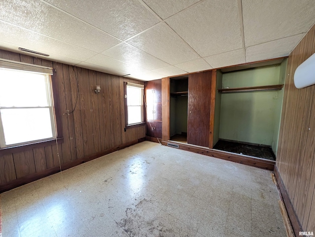 unfurnished bedroom with tile patterned floors, a drop ceiling, wood walls, and baseboards