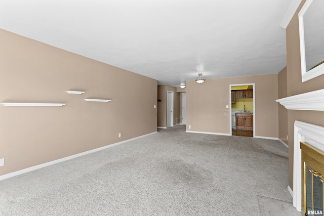 unfurnished living room with a fireplace with flush hearth, baseboards, carpet, and a sink