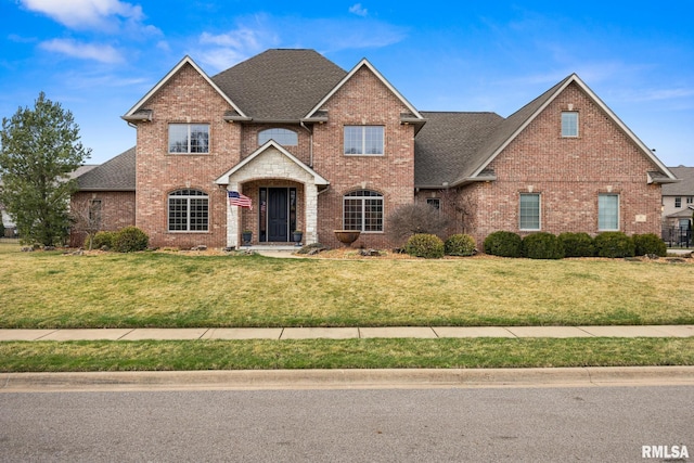 traditional-style house featuring brick siding, a front yard, and a shingled roof