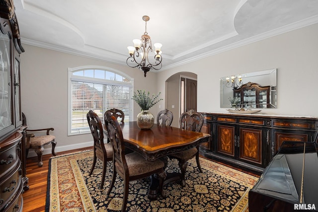 dining space with arched walkways, a notable chandelier, a tray ceiling, and wood finished floors