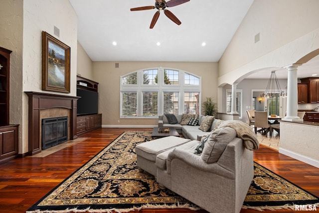 living area featuring arched walkways, ceiling fan, ornate columns, and dark wood-style flooring
