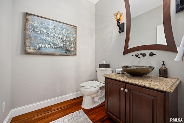 half bath featuring vanity, toilet, wood finished floors, and baseboards