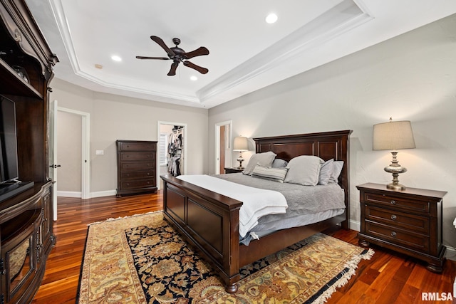 bedroom with a tray ceiling, baseboards, a walk in closet, and dark wood-style flooring