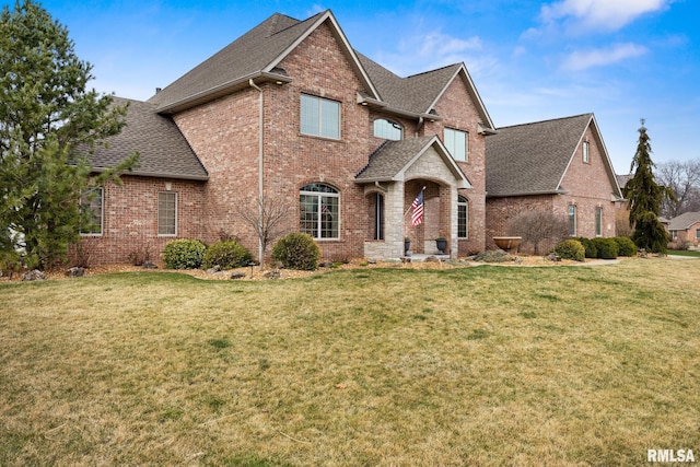 view of front of property featuring brick siding, a shingled roof, and a front lawn