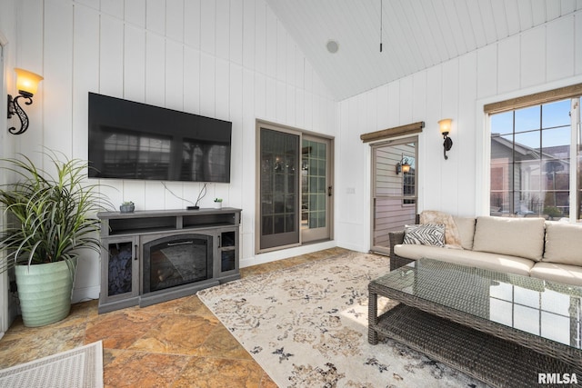 living area with a glass covered fireplace, visible vents, and high vaulted ceiling