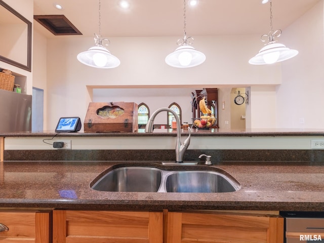 kitchen featuring hanging light fixtures, a sink, dark stone countertops, and visible vents