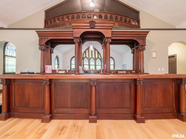 bar featuring light wood-style flooring, lofted ceiling, and arched walkways