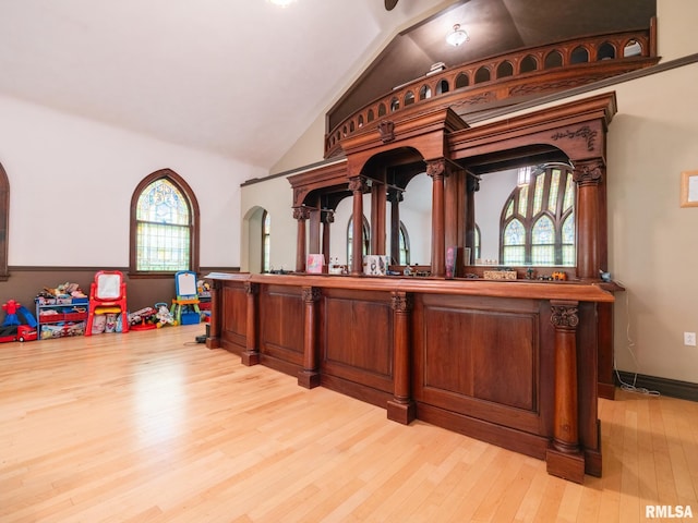 bar featuring baseboards, vaulted ceiling, and light wood-type flooring