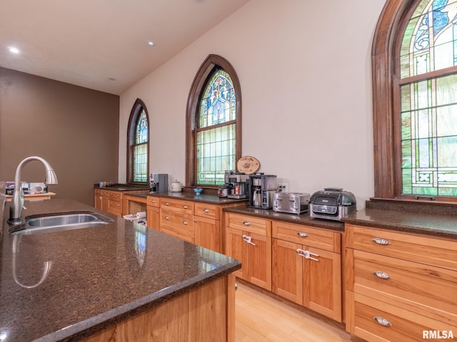 kitchen featuring plenty of natural light, light wood-style flooring, a sink, and dark stone counters