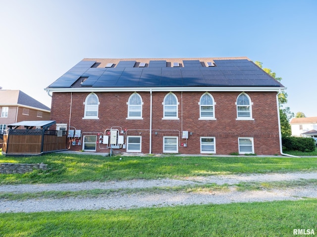 back of property with solar panels, brick siding, and a yard