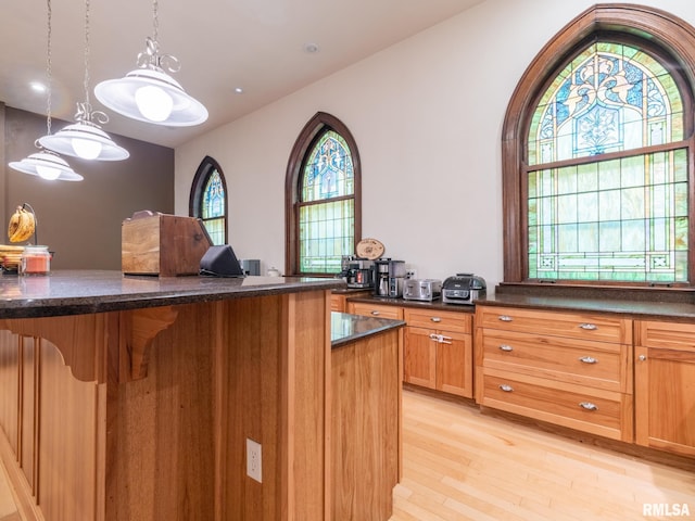 kitchen featuring decorative light fixtures, dark stone counters, light wood-style floors, and a kitchen breakfast bar