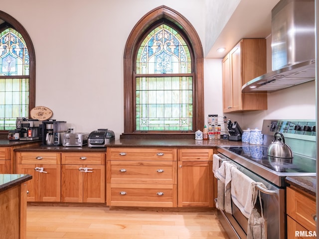 kitchen featuring wall chimney range hood, stainless steel range with electric stovetop, dark countertops, and light wood finished floors