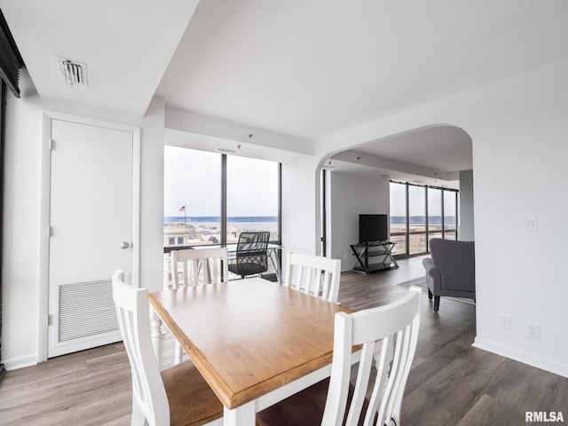dining area featuring baseboards, visible vents, wood finished floors, and arched walkways