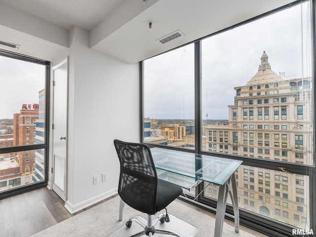 office space featuring visible vents, a city view, baseboards, floor to ceiling windows, and wood finished floors