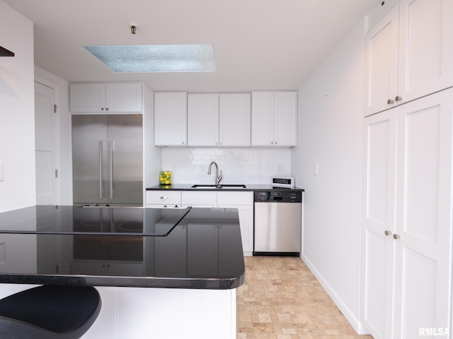 kitchen with backsplash, a sink, dark countertops, white cabinets, and appliances with stainless steel finishes