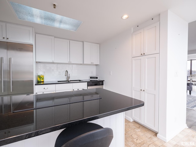 kitchen with white cabinetry, built in refrigerator, decorative backsplash, a sink, and dark countertops