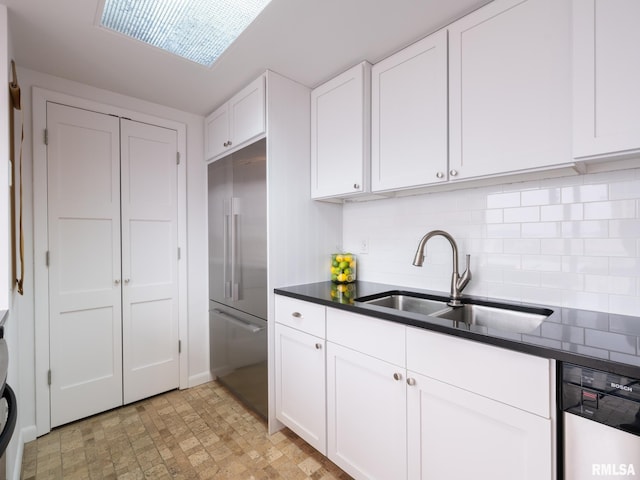kitchen with white cabinets, dark countertops, appliances with stainless steel finishes, a sink, and backsplash