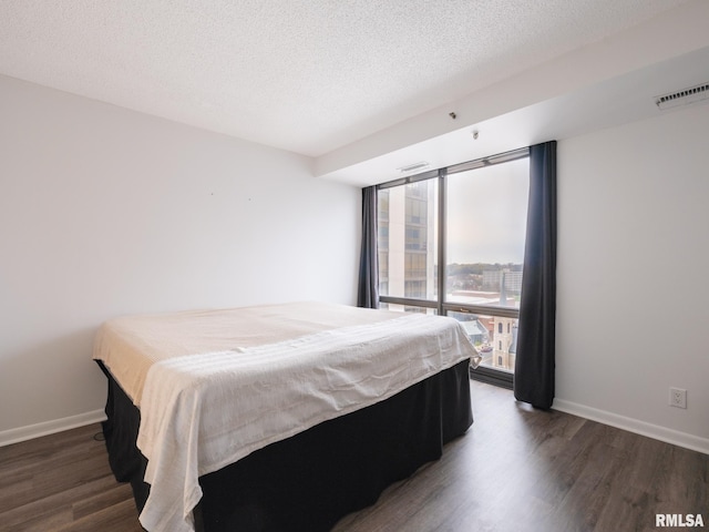 bedroom with wood finished floors, a textured ceiling, baseboards, and visible vents