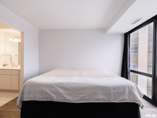 bedroom with a textured ceiling, visible vents, a chandelier, a sink, and light wood-type flooring