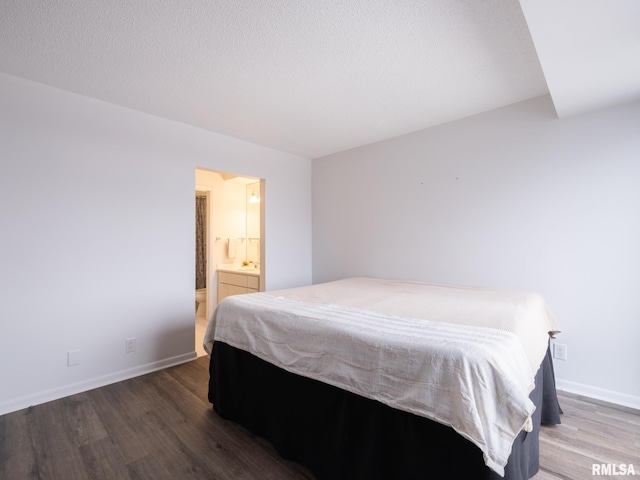 bedroom featuring baseboards, wood finished floors, ensuite bath, and a textured ceiling