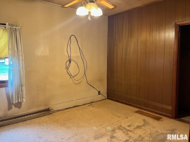 carpeted spare room with baseboard heating, wood walls, a ceiling fan, and visible vents