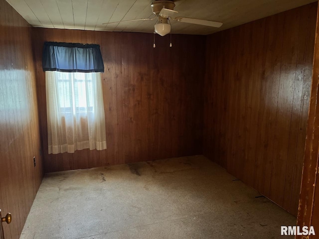 spare room featuring wood walls, a ceiling fan, and carpet