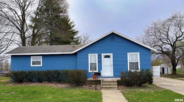 view of front of property featuring a storage shed, roof with shingles, a front yard, and an outdoor structure