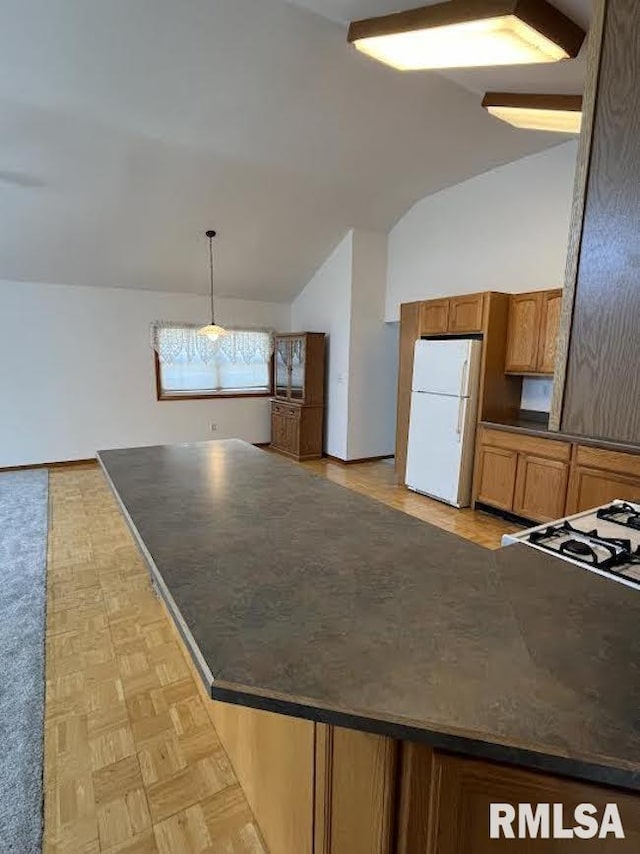 kitchen featuring freestanding refrigerator, dark countertops, vaulted ceiling, brown cabinets, and hanging light fixtures