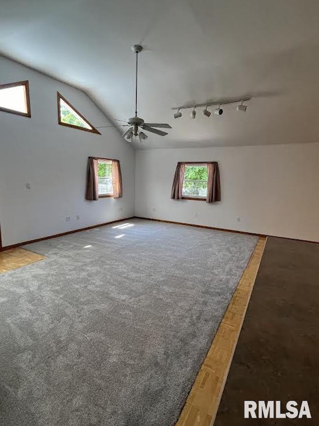 carpeted spare room featuring track lighting, a ceiling fan, vaulted ceiling, and baseboards