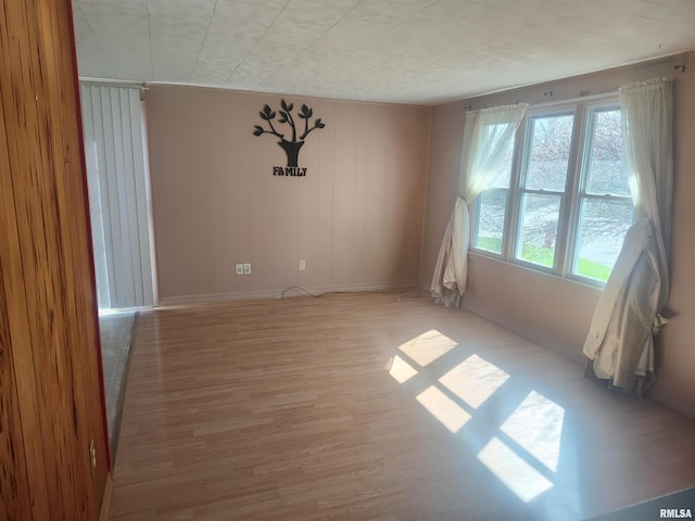 empty room featuring plenty of natural light, light wood-type flooring, and baseboards